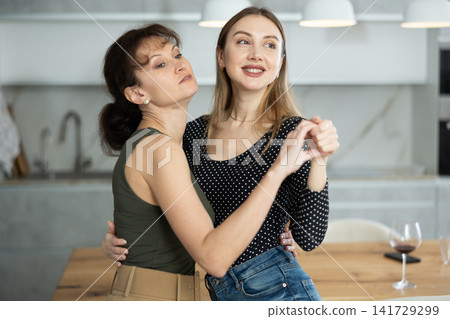 Two joyful middle-aged women dancing together at the kitchen-table with wineglasses Two joyful middle-aged women dancing together at the kitchen-table with wineglasses 141729299