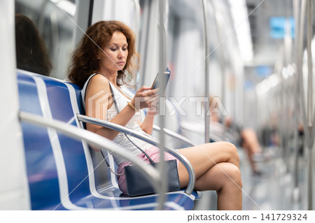 Woman carefully looks at information on a smartphone screen while sitting in subway car 141729324