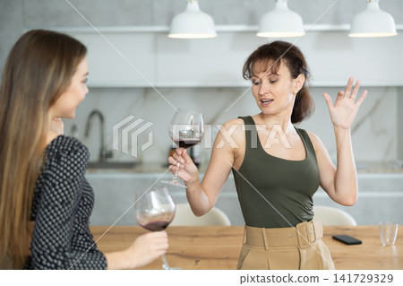 Two joyful middle-aged women dancing together at the kitchen-table with wineglasses Two joyful middle-aged women dancing together at the kitchen-table with wineglasses 141729329