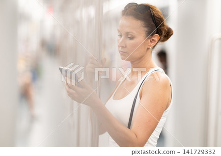 Adult woman standing in subway car with phone Adult woman standing in subway car with phone 141729332
