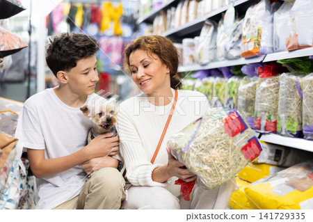 Mom and boy with dog Yorkshire Terrier, take hay from shelf, in pet store. Mom and boy with dog Yorkshire Terrier, take hay from shelf, in pet store. 141729335