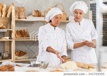 Elderly female baker giving advice to young assistant in kitchen 141729393
