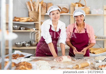 Cheerful women kneading dough together in family bakery Cheerful women kneading dough together in family bakery 141729413