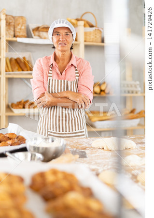 Cheerful aged woman baker in bakehouse Cheerful aged woman baker in bakehouse 141729426