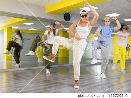Expressive young people practicing new movement in dance with leg out to side in dance room Expressive young people practicing new movement in dance with leg out to side in dance room 141729541