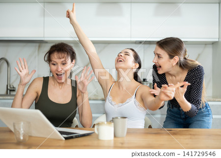 Three happy middle-aged woman expressing joy for winning in the kitchen Three happy middle-aged woman expressing joy for winning in the kitchen 141729546