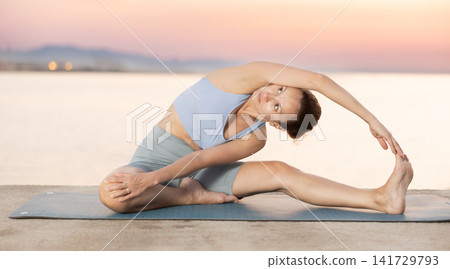 Near sea during sunset, girl performs variations of Janu Shirshasana Near sea during sunset, girl performs variations of Janu Shirshasana 141729793