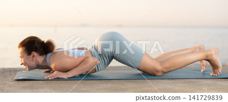 Sportive woman performing cobra pose of yoga during training on beach at sunrise Sportive woman performing cobra pose of yoga during training on beach at sunrise 141729839