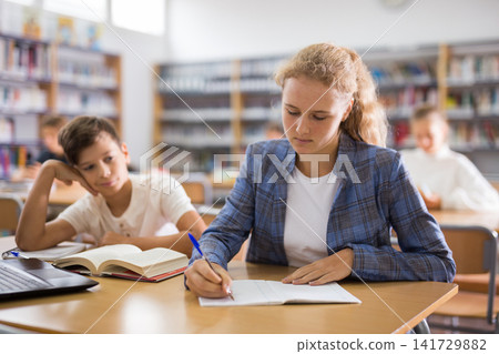 Schoolgirl and schoolboy are sitting together at the same desk at a lesson in school class 141729882
