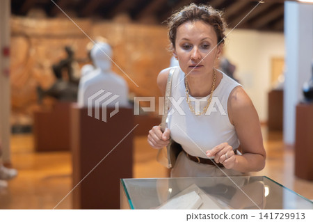 Woman visit museum, examines masterpiece at exhibition Woman visit museum, examines masterpiece at exhibition 141729913