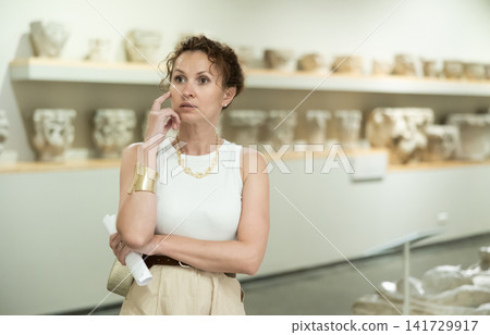 Interested woman examining antique statues in art gallery Interested woman examining antique statues in art gallery 141729917