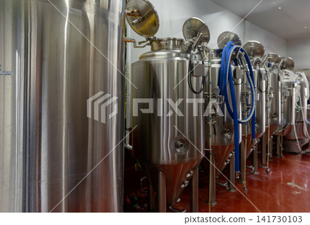 Large stainless steel fermentation tanks lined up in a brewery; image of factory manufacturing equipment. Large stainless steel fermentation tanks lined up in a brewery; image of factory manufacturing equipment. 141730103