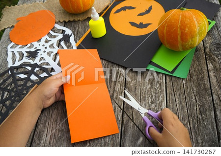 Top view of a child starting a step by step DIY process for creating a Halloween paper decoration Top view of a child starting a step by step DIY process for creating a Halloween paper decoration 141730267