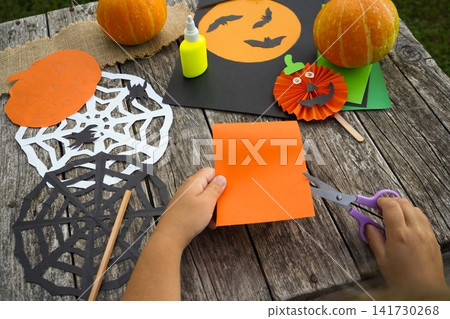 Close up of a kid preparing to make a paper pumpkin craft on a sunny autumn day outdoors Close up of a kid preparing to make a paper pumpkin craft on a sunny autumn day outdoors 141730268