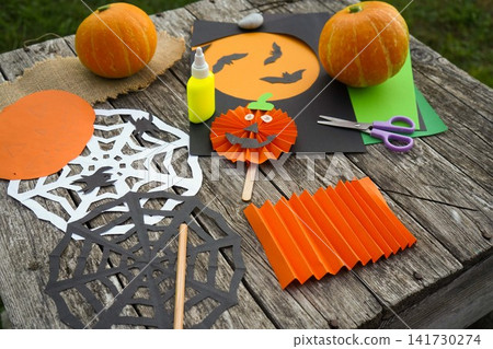 DIY Halloween decorations layout featuring accordion folded orange paper, scissors and liquid glue stick outdoors DIY Halloween decorations layout featuring accordion folded orange paper, scissors and liquid glue stick outdoors 141730274