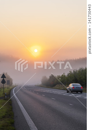 Car driving on foggy road at sunrise in morning Car driving on foggy road at sunrise in morning 141730443