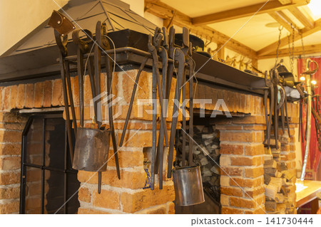 Old metal tools hanging at rustic brick fireplace Old metal tools hanging at rustic brick fireplace 141730444