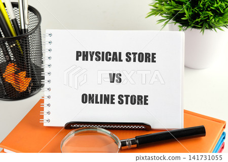 A notebook on a desk shows the words physical store vs online store. A pen and a magnifying glass sit nearby, with a plant in the background A notebook on a desk shows the words physical store vs online store. A pen and a magnifying glass sit nearby, with a plant in the background 141731055