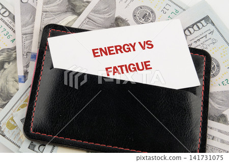 A black wallet is open with a card that reads energy vs fatigue. Surrounding the wallet are several stacks of US dollar bills. The scene shows a financial theme A black wallet is open with a card that reads energy vs fatigue. Surrounding the wallet are several stacks of US dollar bills. The scene shows a financial theme 141731075