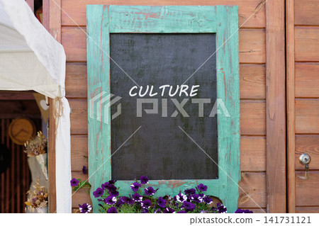 A sign with the word culture is placed on a wooden wall. Purple flowers grow near the base of the sign. The image shows a bright atmosphere in a public space A sign with the word culture is placed on a wooden wall. Purple flowers grow near the base of the sign. The image shows a bright atmosphere in a public space 141731121