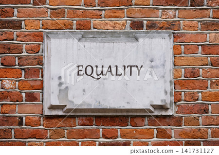 A sign is mounted on a brick wall in a public area. The word equality is displayed clearly on the sign. The setting is bright and open during the day A sign is mounted on a brick wall in a public area. The word equality is displayed clearly on the sign. The setting is bright and open during the day 141731127