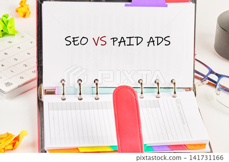 A planner is open with notes comparing seo and paid ads. Colorful tabs are visible. This setup is on a desk with office supplies scattered around A planner is open with notes comparing seo and paid ads. Colorful tabs are visible. This setup is on a desk with office supplies scattered around 141731166