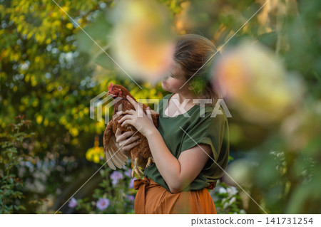 Young farmer holding a hen in the garden. Chicken hen was held by female owner in backyard garden. Young farmer holding a hen in the garden. Chicken hen was held by female owner in backyard garden. 141731254