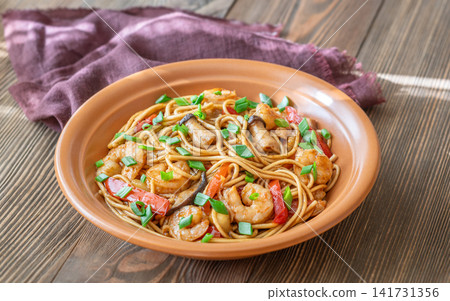 Asian stir fry udon noodles with prawns mushrooms vegetables in rustic ceramic bowl Asian stir fry udon noodles with prawns mushrooms vegetables in rustic ceramic bowl 141731356