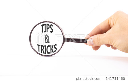Tips and tricks words symbol. Concept words Tips and tricks on beautiful magnifying glass. Beautiful white background. Businessman hand. Business tips tricks motivational support concept. Copy space. Tips and tricks words symbol. Concept words Tips and tricks on beautiful magnifying glass. Beautiful white background. Businessman hand. Business tips tricks motivational support concept. Copy space. 141731460