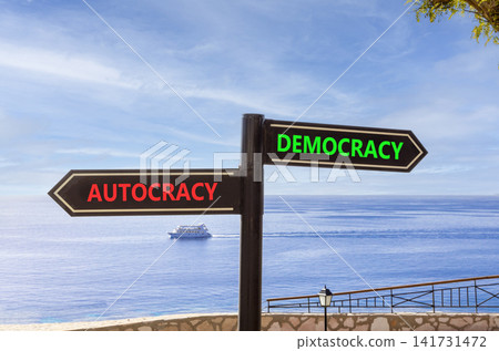 Democracy or autocracy words symbol. Concept words Democracy Autocracy on beautiful black road sign. Beautiful blue sky background. Business democracy autocracy concept. Copy space Democracy or autocracy words symbol. Concept words Democracy Autocracy on beautiful black road sign. Beautiful blue sky background. Business democracy autocracy concept. Copy space 141731472