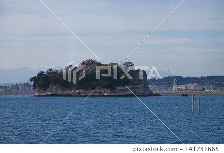 A serene view of a small islet surrounded by calm waters, with distant urban structures and mountains under a partly cloudy sky. A serene view of a small islet surrounded by calm waters, with distant urban structures and mountains under a partly cloudy sky. 141731665