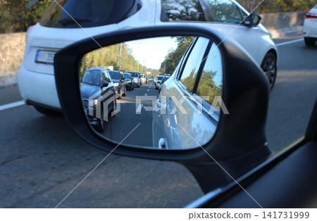 Heavy traffic takes up all lanes on a country road. View of a traffic jam in a car mirror with blurred vehicles on a road Heavy traffic takes up all lanes on a country road. View of a traffic jam in a car mirror with blurred vehicles on a road 141731999