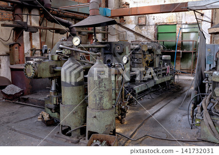 Heavy industrial machine with hydraulic pressure cylinders and gauges inside an old metal processing workshop Heavy industrial machine with hydraulic pressure cylinders and gauges inside an old metal processing workshop 141732031