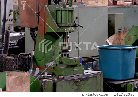 Green industrial hydraulic press machine on dirty workbench with blue bucket inside manufacturing workshop Green industrial hydraulic press machine on dirty workbench with blue bucket inside manufacturing workshop 141732053