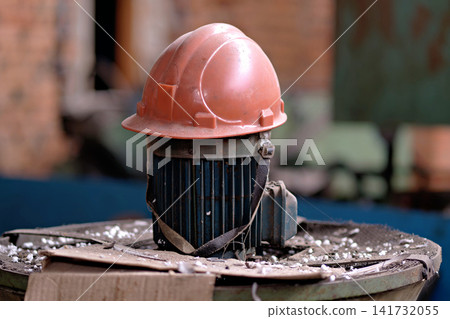 Orange hard hat safety helmet placed on vintage electric motor inside industrial factory building Orange hard hat safety helmet placed on vintage electric motor inside industrial factory building 141732055