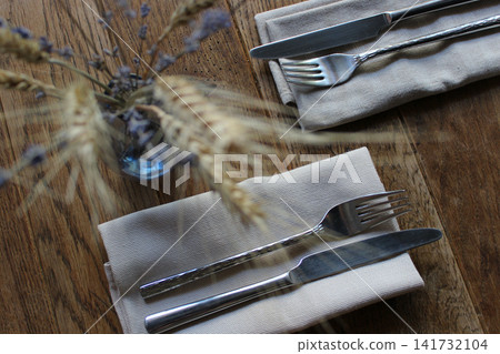 Vintage family restaurant table with forks and knives on yarn napkins and vase with ornamental bouquet of wheat ears and lavender sprigs soft focus Vintage family restaurant table with forks and knives on yarn napkins and vase with ornamental bouquet of wheat ears and lavender sprigs soft focus 141732104