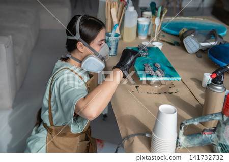 Talented woman artist creating liquid art painting, holding stick and adding drops of epoxy resin. Talented woman artist creating liquid art painting, holding stick and adding drops of epoxy resin. 141732732