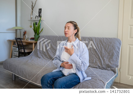 Positive mature woman practicing stress relief and deep breathing self helping therapy at home. Positive mature woman practicing stress relief and deep breathing self helping therapy at home. 141732801