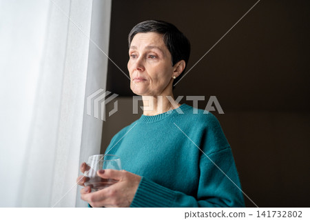 Exhausted woman with water medicine by window in stillness alone. Emotional tress, quiet reflection Exhausted woman with water medicine by window in stillness alone. Emotional tress, quiet reflection 141732802