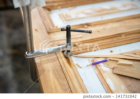 Clamp tool fixed over vintage wooden door part securing details together during restoration process. Clamp tool fixed over vintage wooden door part securing details together during restoration process. 141732842