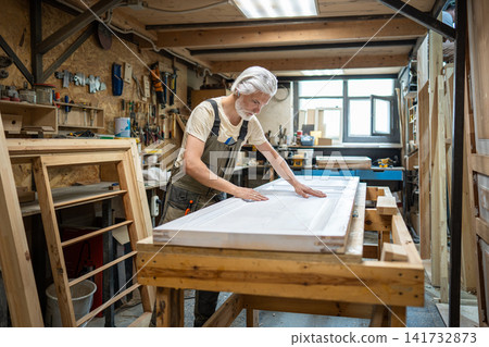 Woodworking master in restoration workshop precisely checking condition of old interior wooden door. Woodworking master in restoration workshop precisely checking condition of old interior wooden door. 141732873