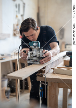 Concentrated master carpenter using handheld wood router instrument in restoration workshop. Concentrated master carpenter using handheld wood router instrument in restoration workshop. 141732886
