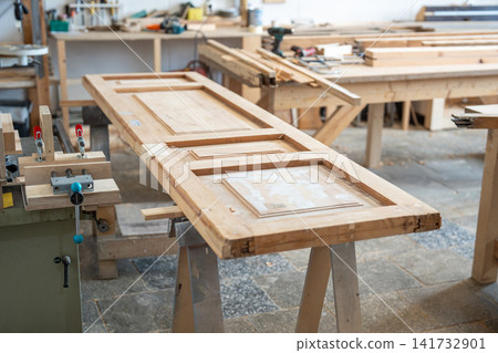 Renovation process in restoration workshop, antique wooden door lying at workbench in carpentry Renovation process in restoration workshop, antique wooden door lying at workbench in carpentry 141732901