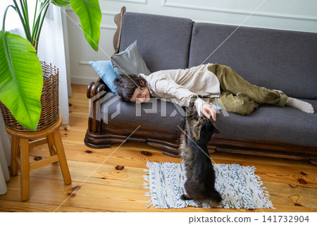 Cheerful woman playing with cat while fully relaxing on couch in room, happiness at home on weekend. Cheerful woman playing with cat while fully relaxing on couch in room, happiness at home on weekend. 141732904