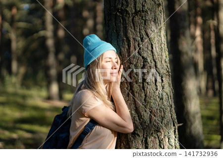 Carefree mature woman hiking in forest alone, standing lean to tree enjoying peaceful moment. Carefree mature woman hiking in forest alone, standing lean to tree enjoying peaceful moment. 141732936