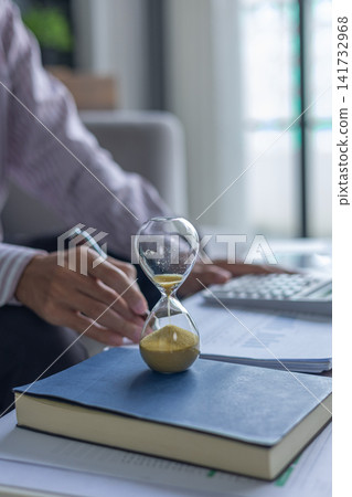 Business Consultant Analyzing Data Sheets and Financial Charts at Desk with Hourglass on Table. Time Management Concept. Business Consultant Analyzing Data Sheets and Financial Charts at Desk with Hourglass on Table. Time Management Concept. 141732968