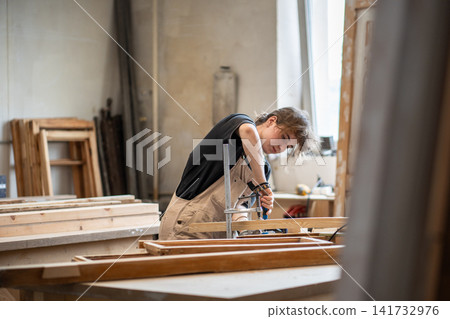 Skillful woman restorer working with wooden details and tools at workbench in restoration workshop Skillful woman restorer working with wooden details and tools at workbench in restoration workshop 141732976