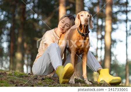Recreation, building relationships and trust with pet, tranquil woman relaxing in forest with dog. Recreation, building relationships and trust with pet, tranquil woman relaxing in forest with dog. 141733001