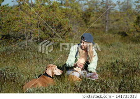 Cheerful woman forager with dog gathering wild berries and herbs at marshland in wild forest. Cheerful woman forager with dog gathering wild berries and herbs at marshland in wild forest. 141733038