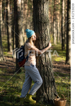 Connection with nature and mindfulness, happy relaxed woman hugs tree trunk in forest on solo trip. Connection with nature and mindfulness, happy relaxed woman hugs tree trunk in forest on solo trip. 141733039